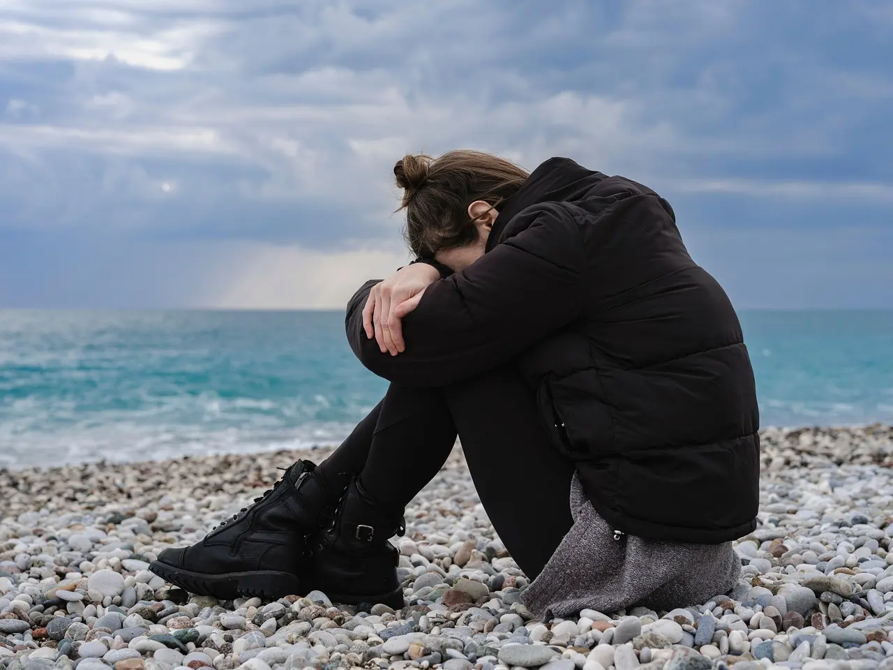 Personne seule au bord de l'eau, assise au sol, genoux pliés et la tête entre les bras